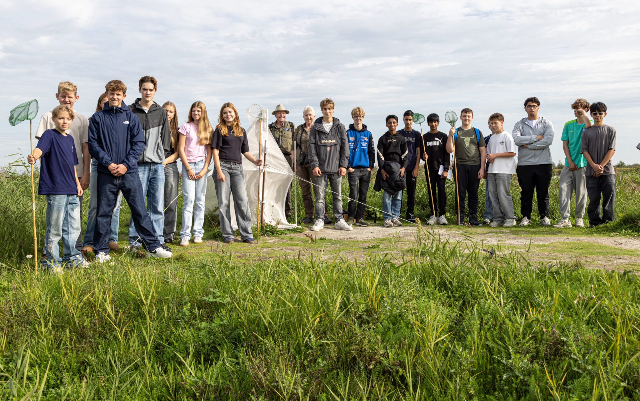 Groep mensen met netten staat op een grasland onder een bewolkte hemel.