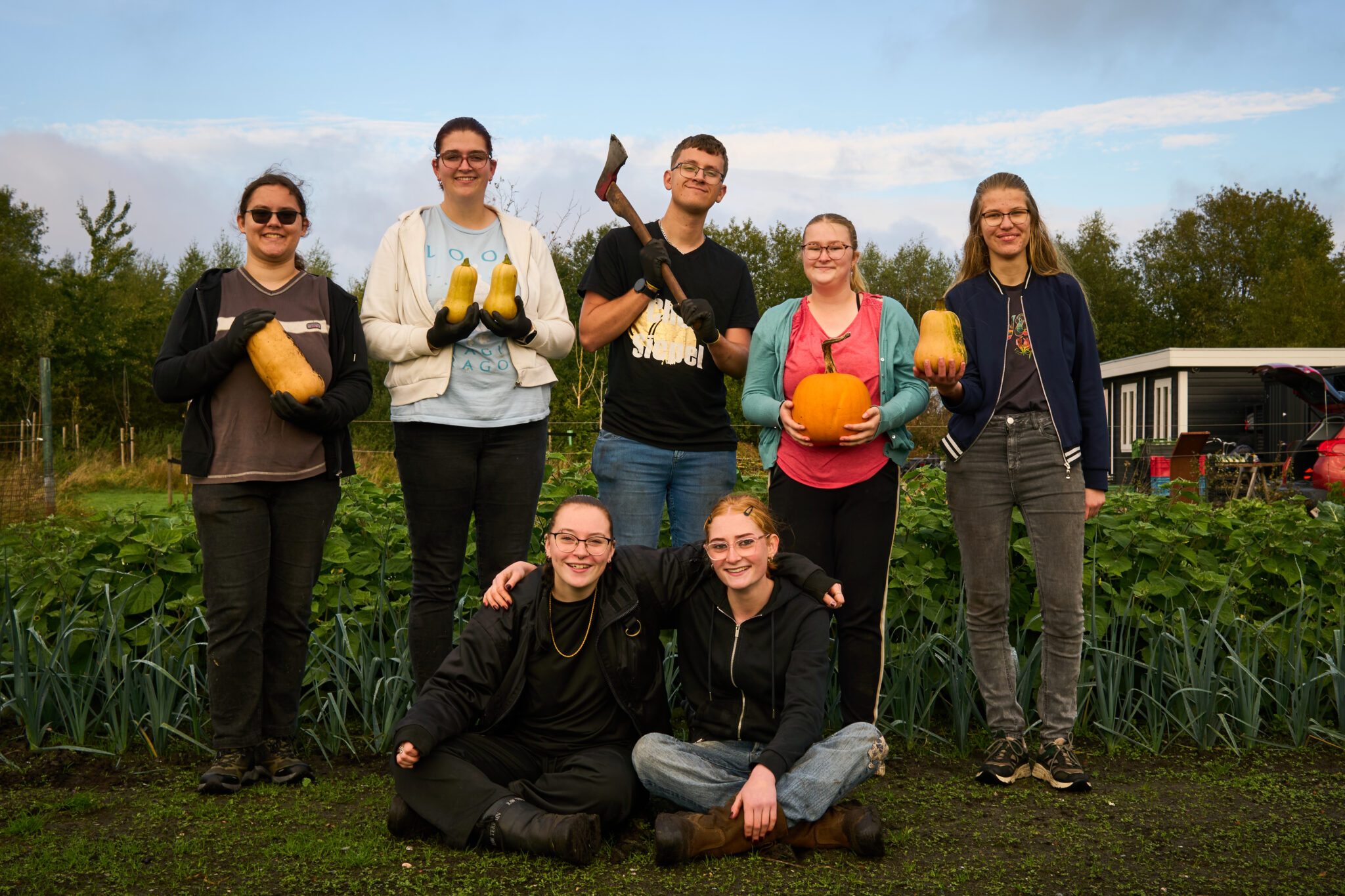 groep deelnemers poseren met pompoenen in de moestuin