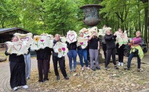 Groep mensen toont versierde stoffen met harten en bloemen, in een bosrijke omgeving.