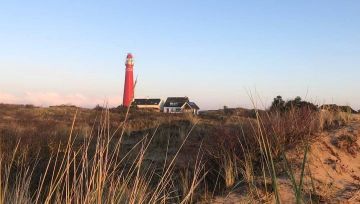 Rode vuurtoren en huizen op duin, omringd door gras bij zonsondergang.