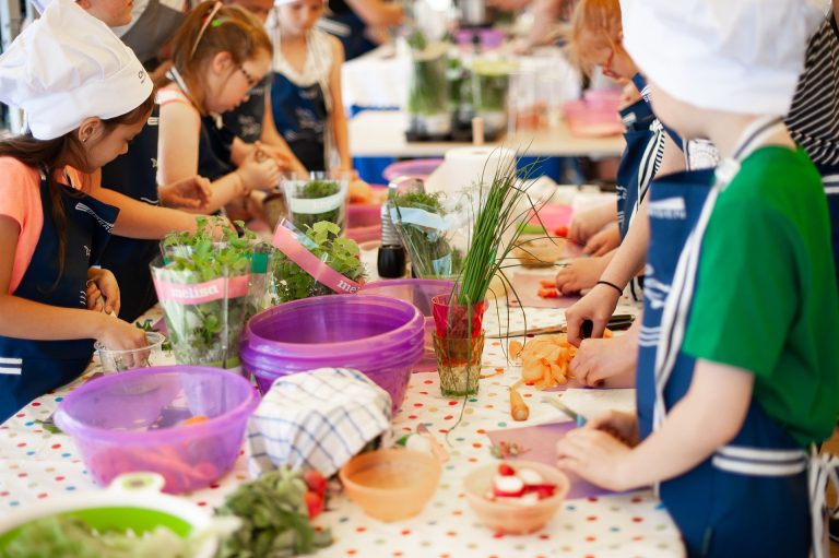 Kinderen koken samen aan een tafel, omringd door groenten en kruiden.