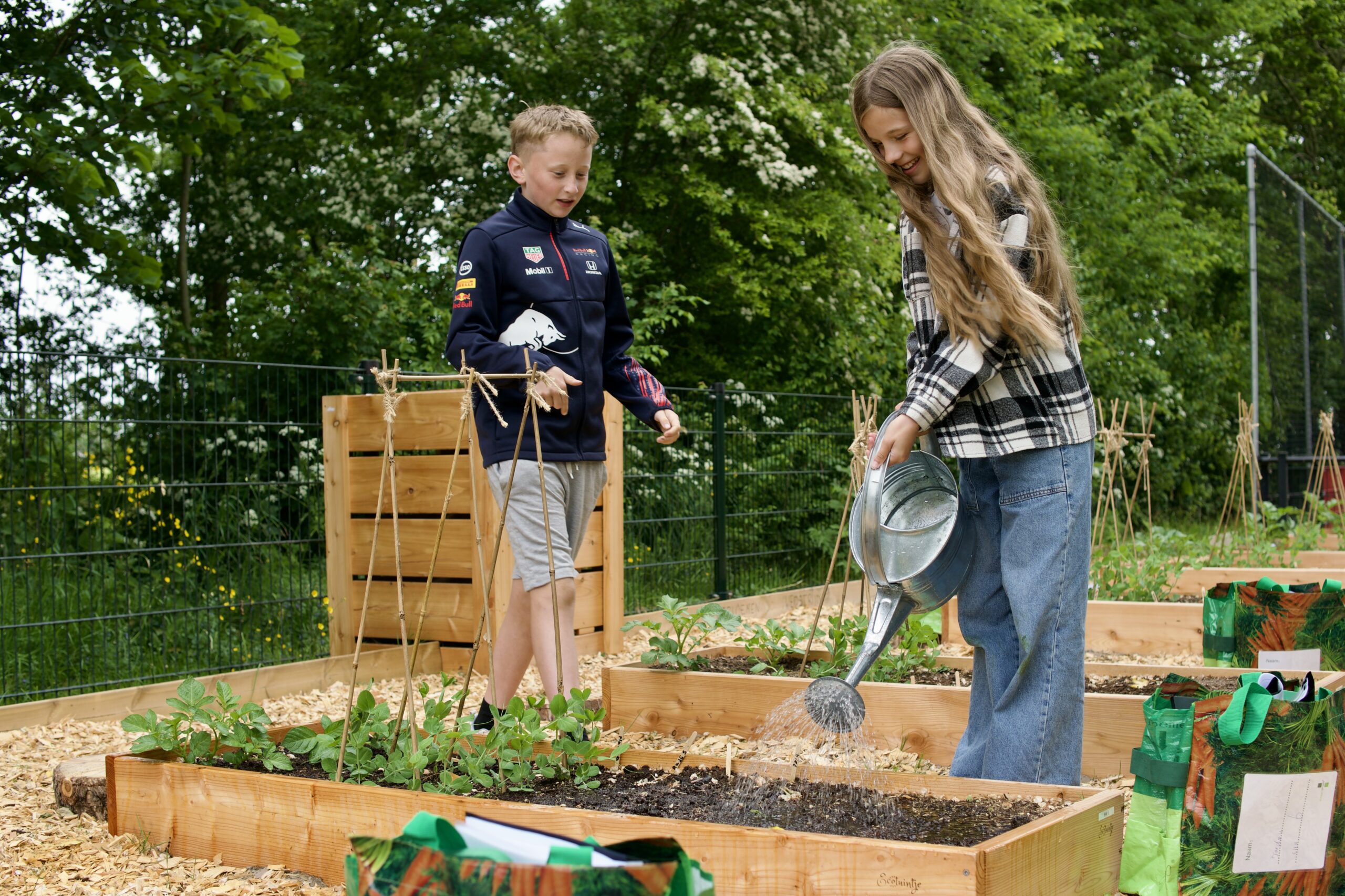 Kinderen verzorgen planten in een moestuin met houten bakken en een gieter.
