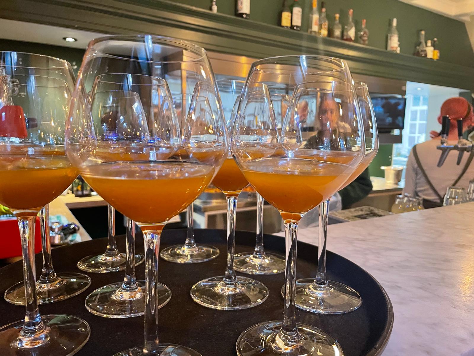 Glazen met oranje cocktails op een dienblad, op een bar met flessen op de achtergrond.