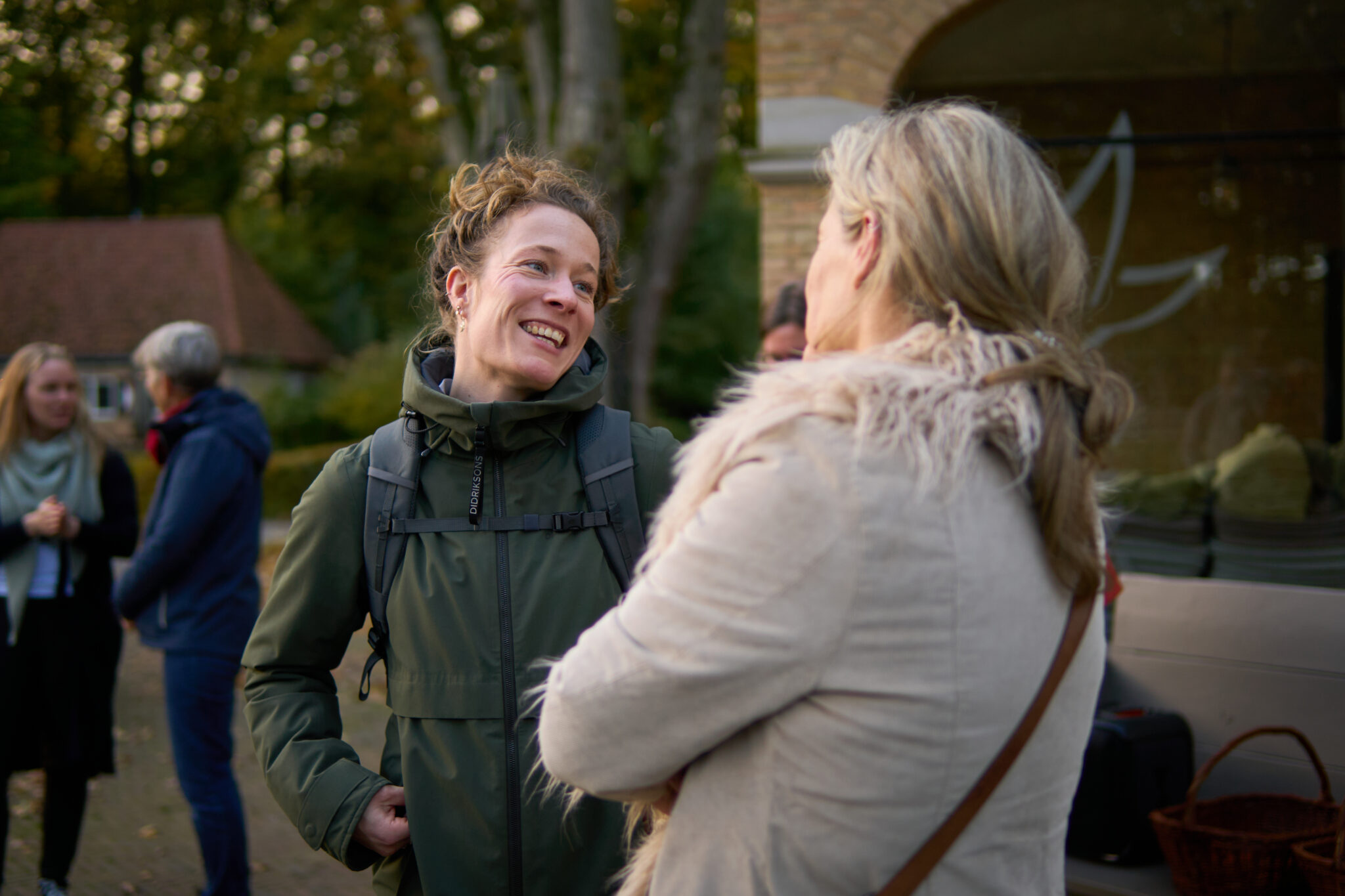 Twee vrouwen praten vrolijk buiten, met anderen onscherp op de achtergrond.