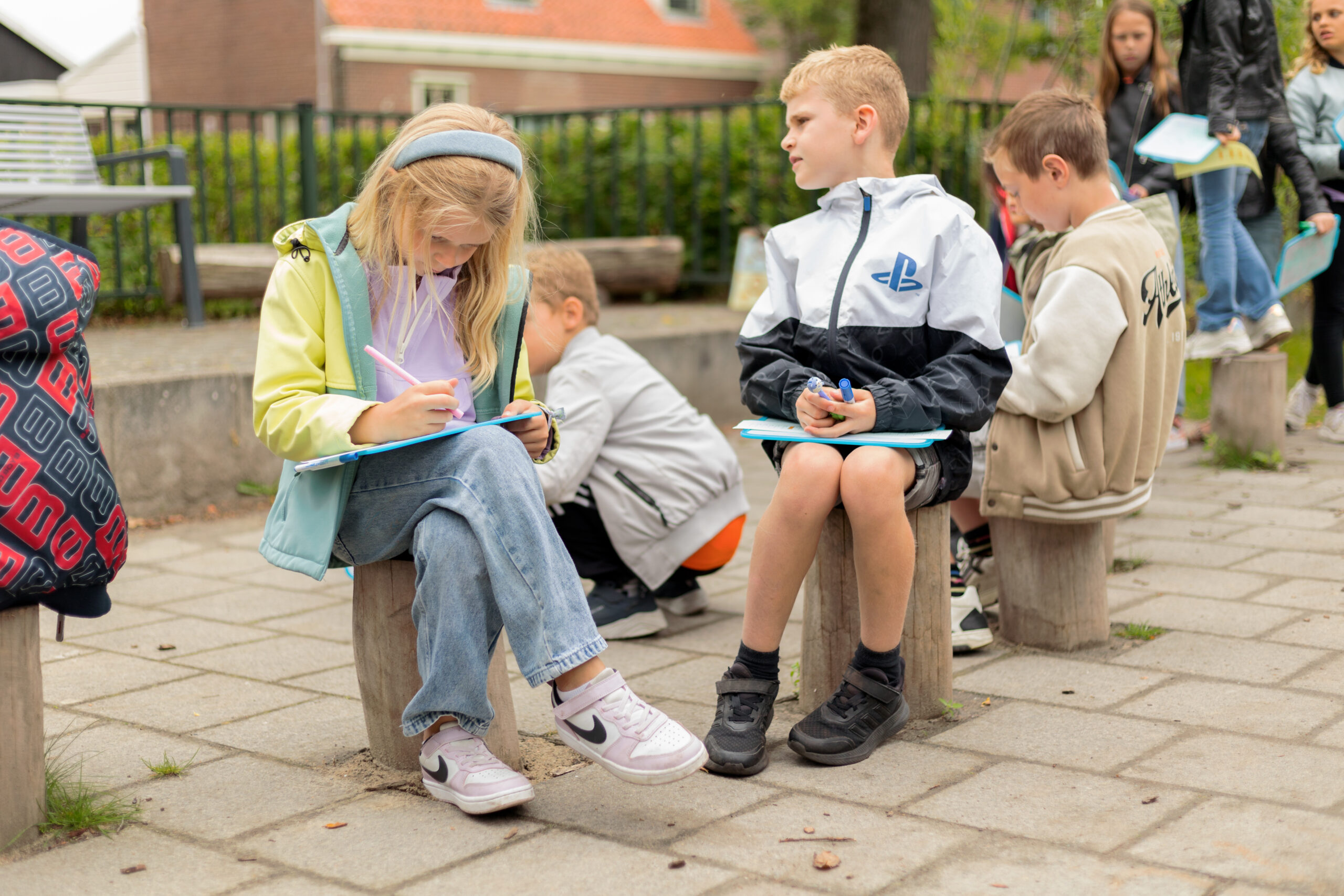 Kinderen zitten buiten op boomstammen en schrijven op klemborden.