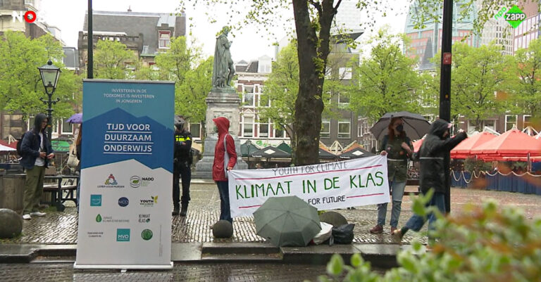 Protest voor duurzaam onderwijs en klimaat in de klas; mensen met spandoeken en paraplu's.