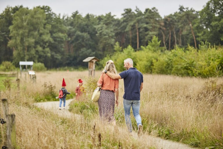 Een stel wandelt over een pad in een natuurgebied, gevolgd door kinderen met rode puntmutsen.