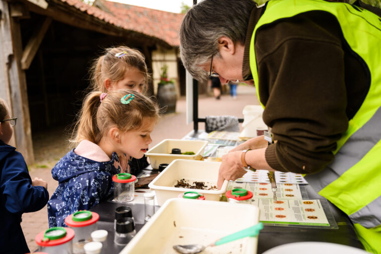 Volwassene toont kinderen organisch materiaal bij een educatieve tafel buiten.