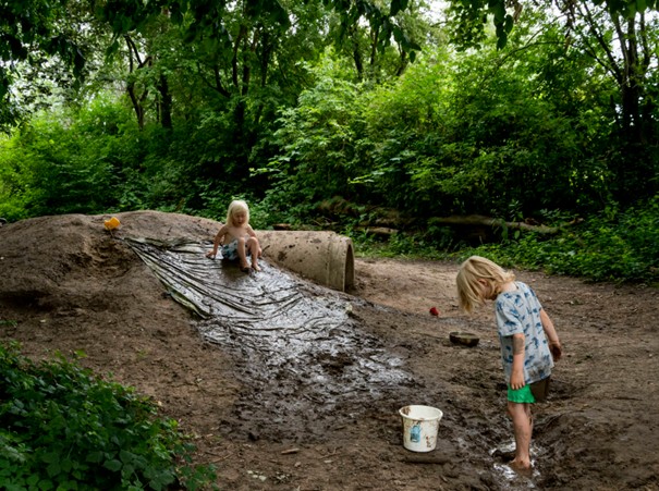 Twee kinderen spelen op een modderige heuvel in een groen bos.