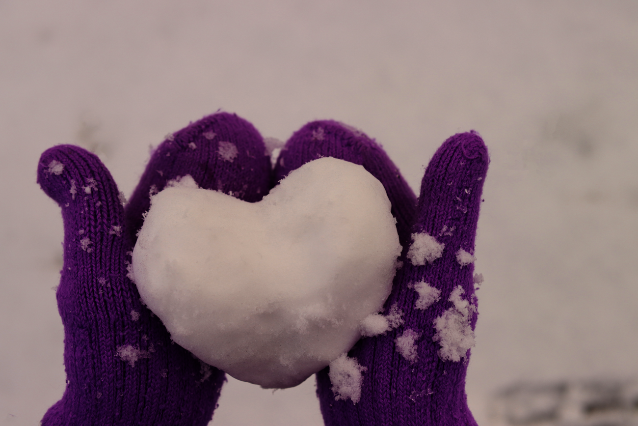 Paarse handschoenen houden een hartvormige sneeuwbal vast.