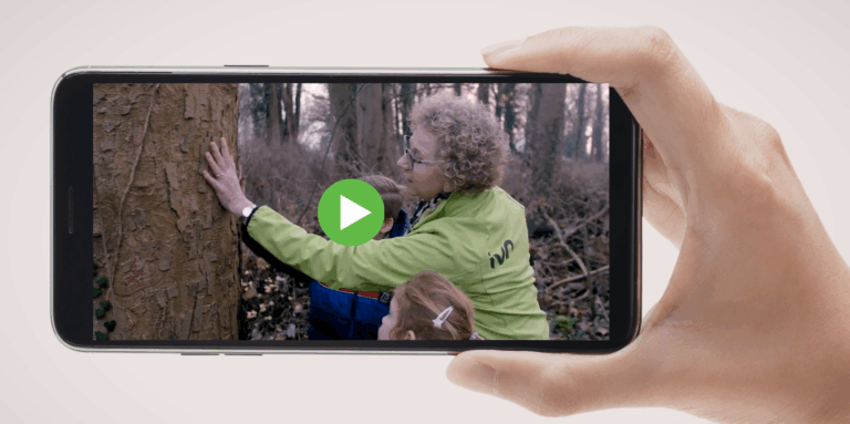 Hand houdt smartphone met video afspelen-symbool, toont persoon en kind bij boom in bos.