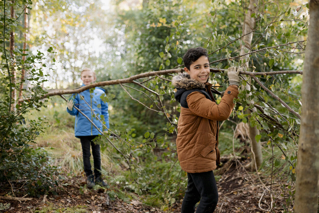Twee kinderen slepen een tak door het bos.