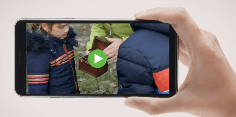 Kind open een houten doos buiten op een smartphone-scherm met afspeelknop.