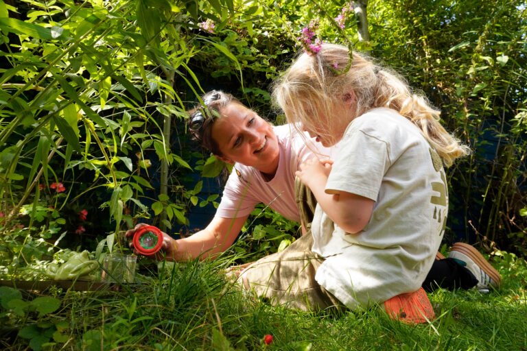 Twee mensen onderzoeken planten in een zonnige tuin, omringd door groene bladeren.