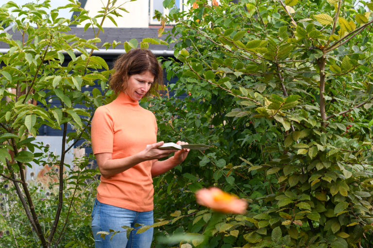 Vrouw in oranje trui leest een boek in een groene tuin.