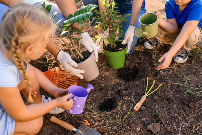 Kinderen planten samen bloemen in de tuin, met handschoenen en gieters.