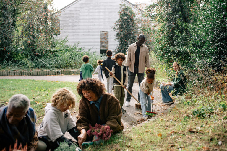 Mensen van verschillende leeftijden werken samen in een tuin, planten en vegen bladeren.
