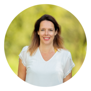 Een vrouw in een witte blouse poseert buiten met een wazige groene achtergrond.