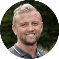Man glimlacht naar de camera, groen wazige achtergrond.