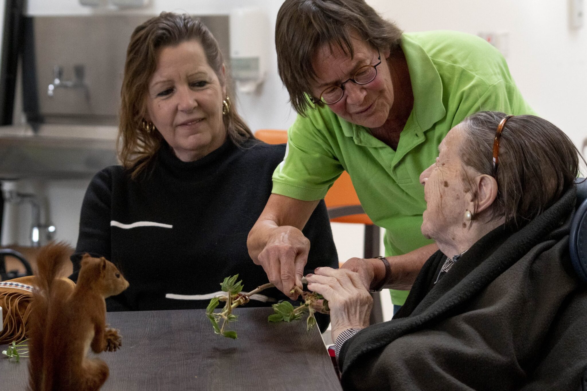 Drie mensen interageren met een eekhoorn en planten aan een tafel.