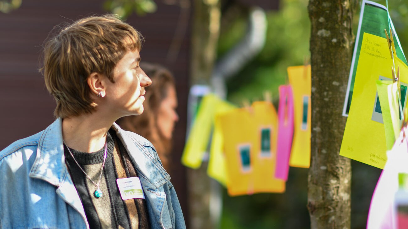 Persoon kijkt naar kleurige papieren die aan een waslijn hangen, buiten in zonlicht.