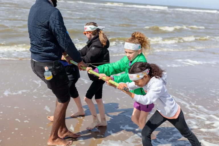 Kinderen en volwassene spelen touwtrekken op het strand bij de zee.