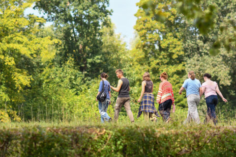 Mensen wandelen in een groene bosrijke omgeving, lichte zomerkleding.