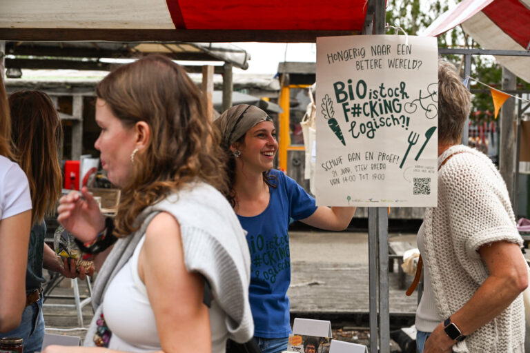 Vrouwen bij een marktstand met een poster over biologische producten en een proefevenement.