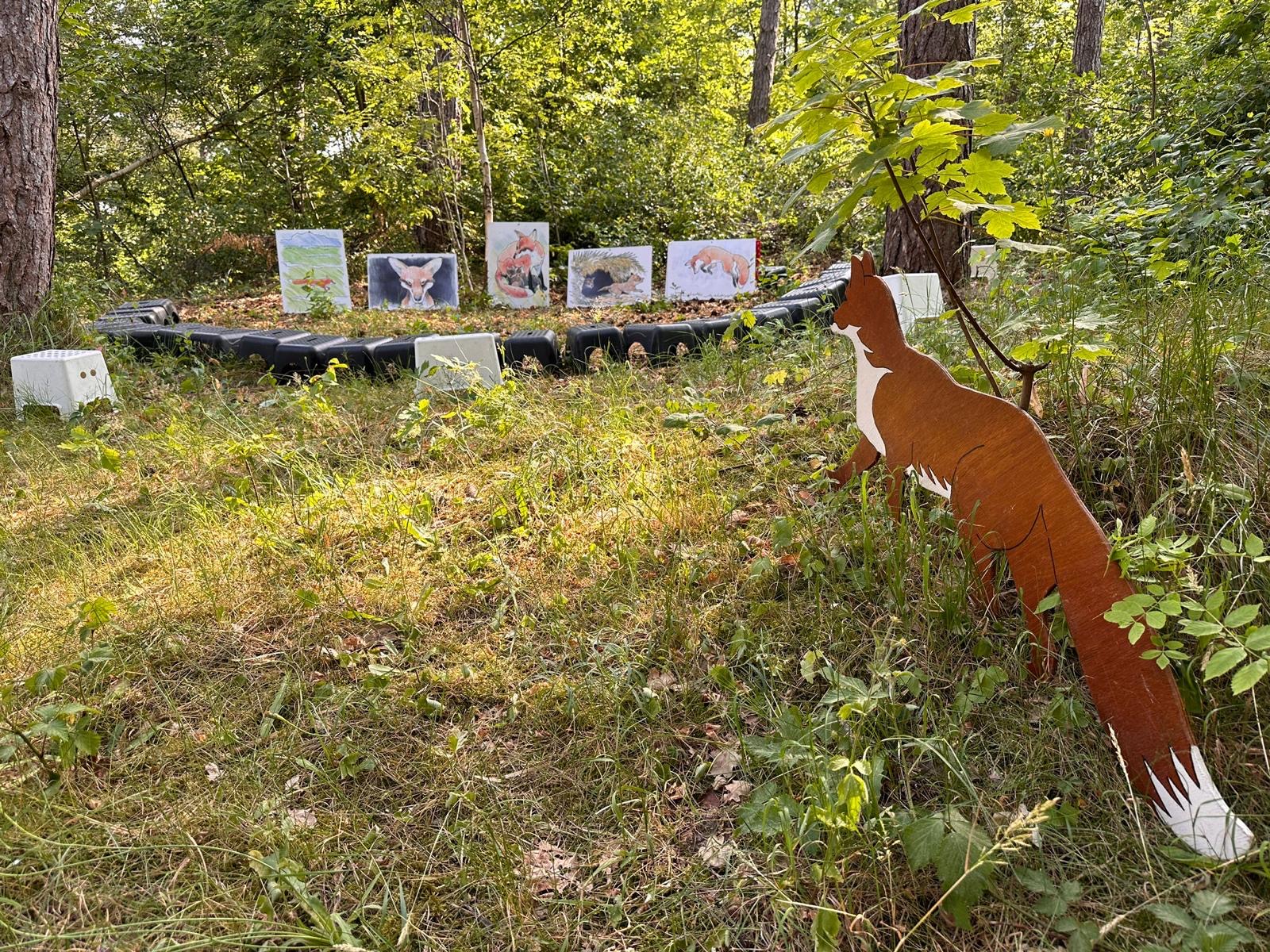 Houten vosbeeld in bos, met schilderijen op achtergrond.