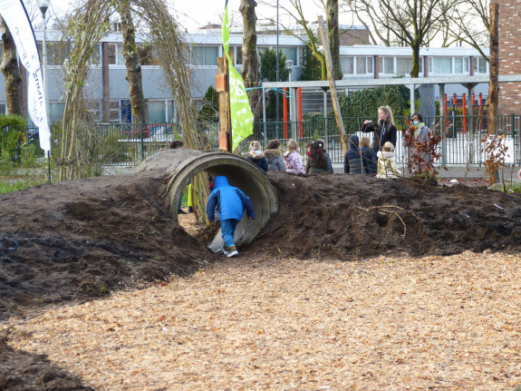 Een kleine jongen loopt gebukt door een rioolbuis naar de rest van zijn klas toe. Zij bekijken het Tiny Forest in aanplant. 