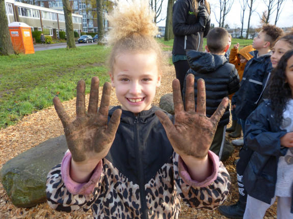Meisje laat met een grote glimlach haar modderige handen zien na het bomen planten in het Tiny Forest. 
