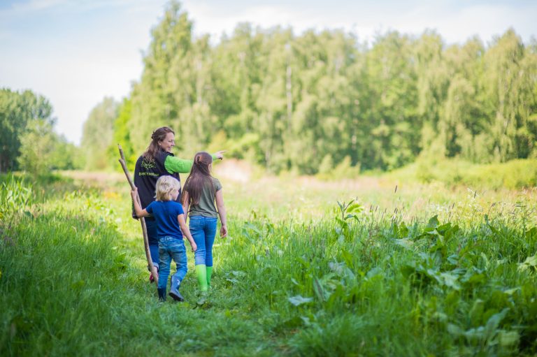 Drie mensen wandelen in een groen natuurgebied, één wijst iets aan in de verte.