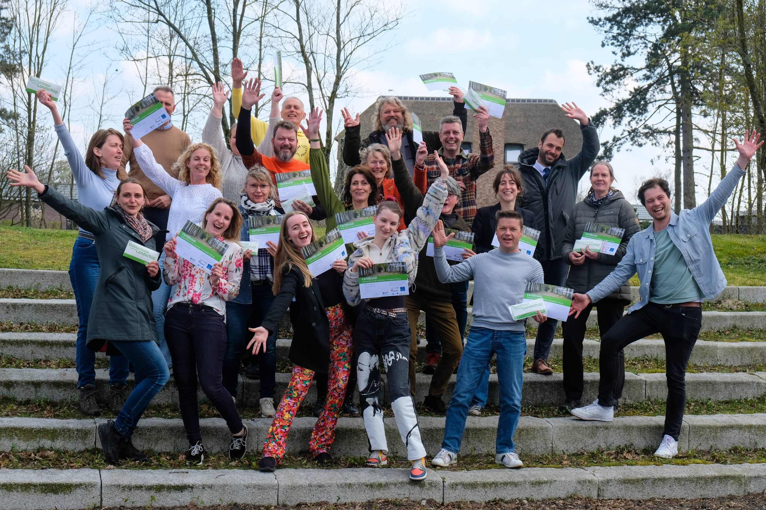 Groep mensen viert buiten op trappen, lachend en met certificaten in de hand.