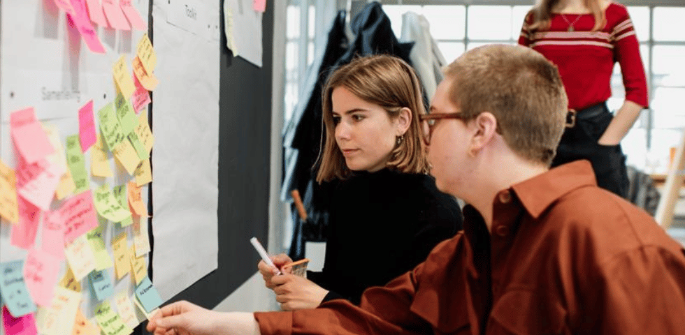 Twee mensen bekijken een muur vol gekleurde sticky notes.