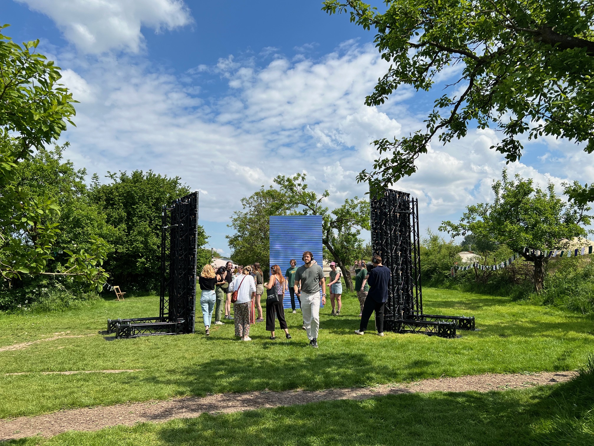 Een groep mensen verzamelt zich bij een grote, openlucht installatie in een groene parkachtige omgeving.