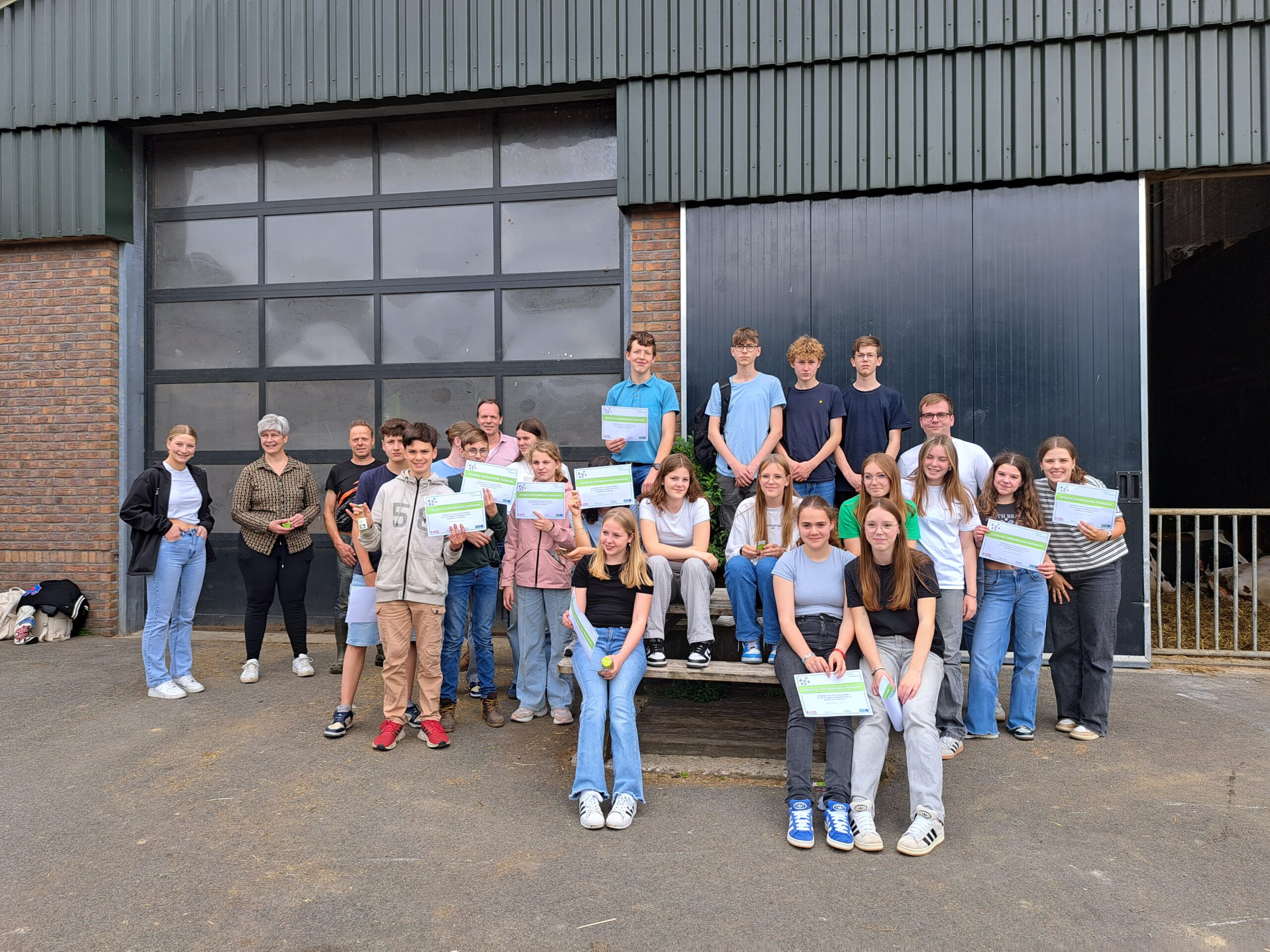 Groep jongeren poseert voor een gebouw met certificaten in hun handen.