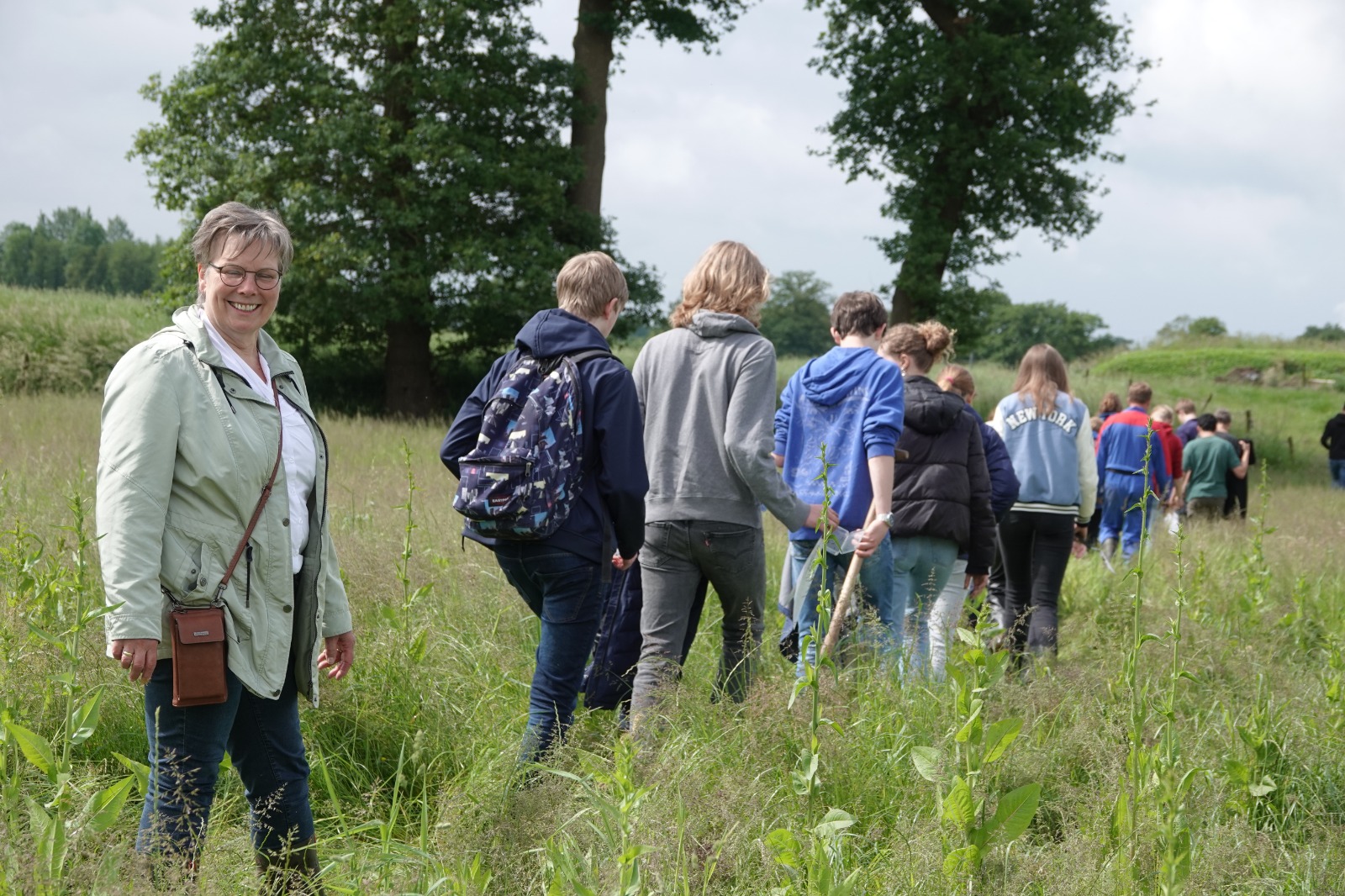 Groep mensen wandelt door een grasveld; vrouw glimlacht naar de camera.