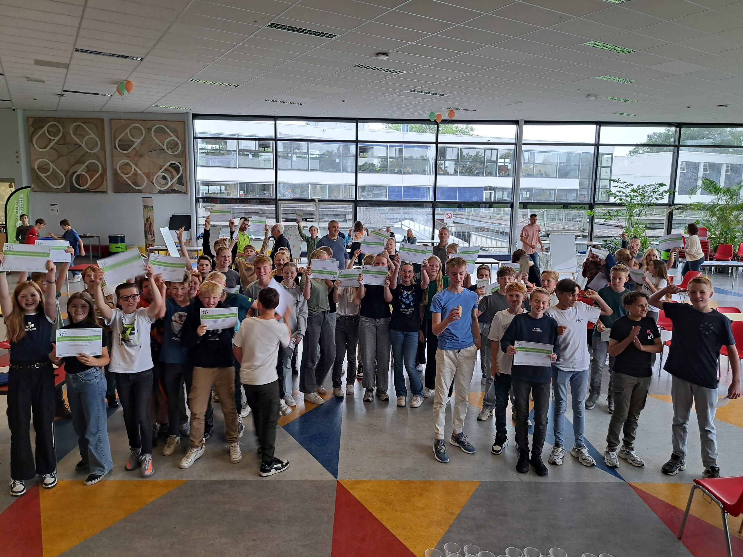 Een groep blije jongeren in een zaal toont certificaten.