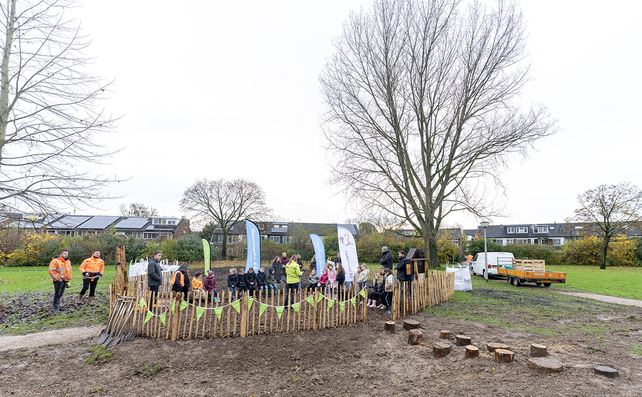 Mensen verzamelen zich bij een omheind gebied in een park met spandoeken en schoppen.
