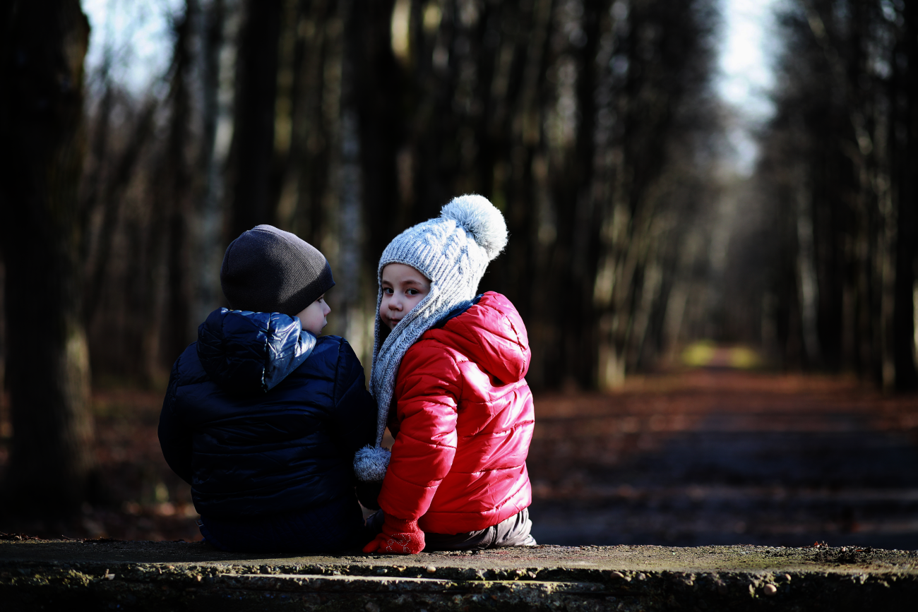 Twee kinderen in warme jassen zitten op een bankje in een winterbos.