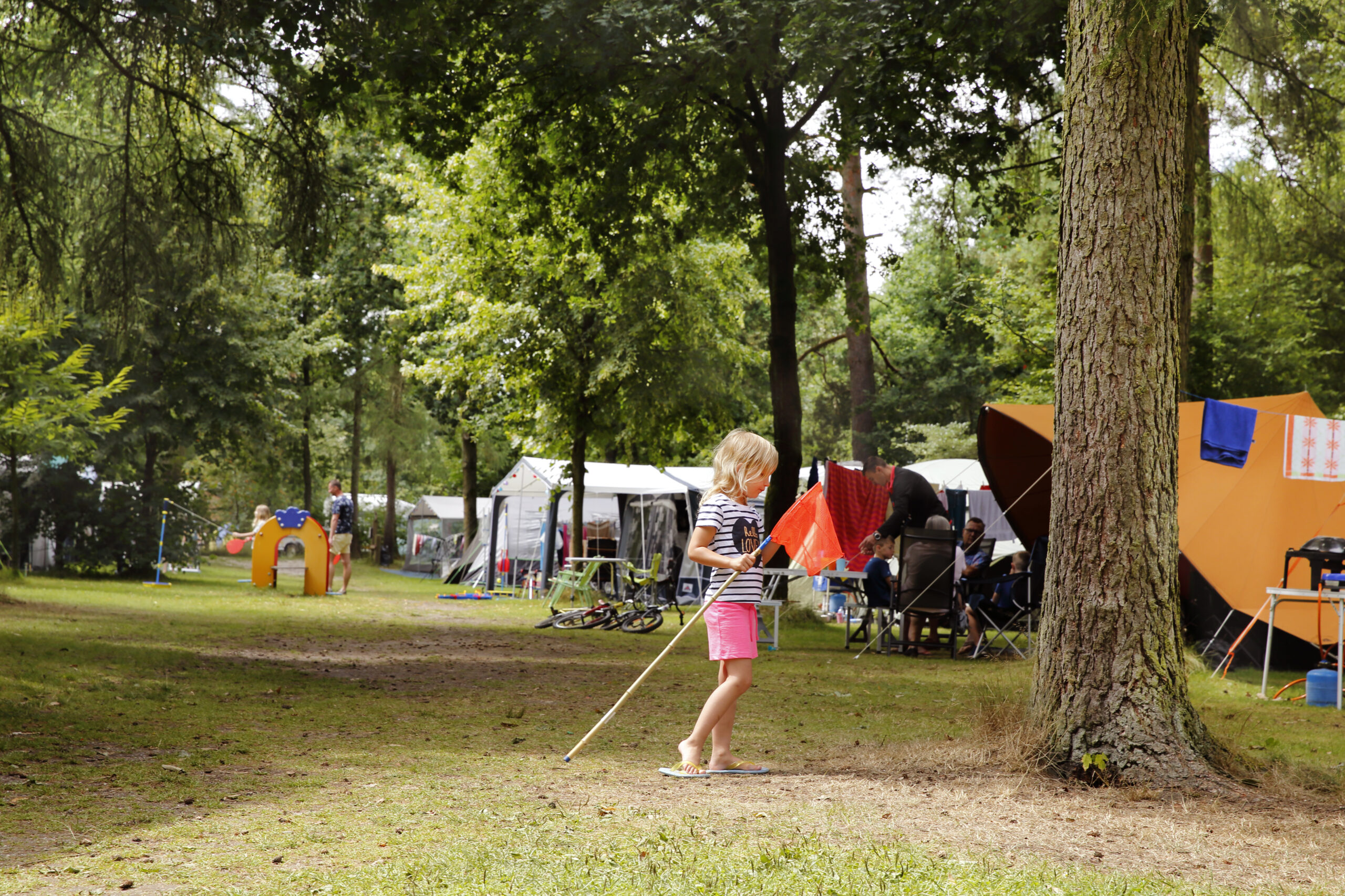 Kind speelt met vlag op een camping met tenten en bomen op de achtergrond.