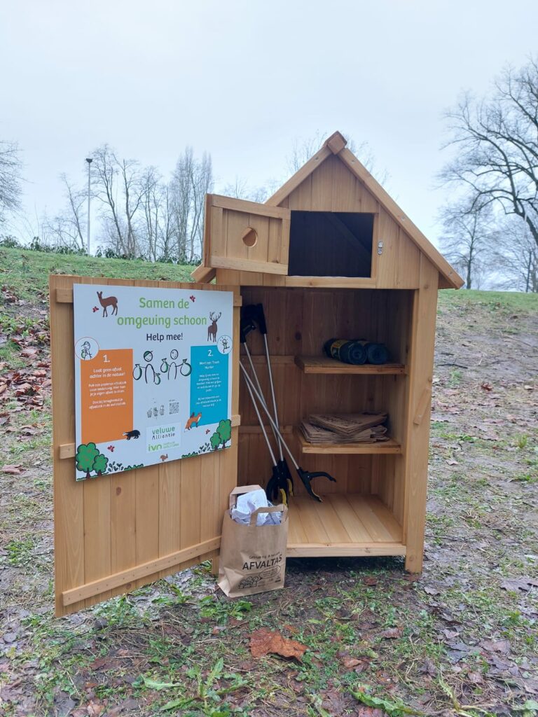 Houten kast in park met prikkers, afvaltas en poster voor zwerfafval opruimen.