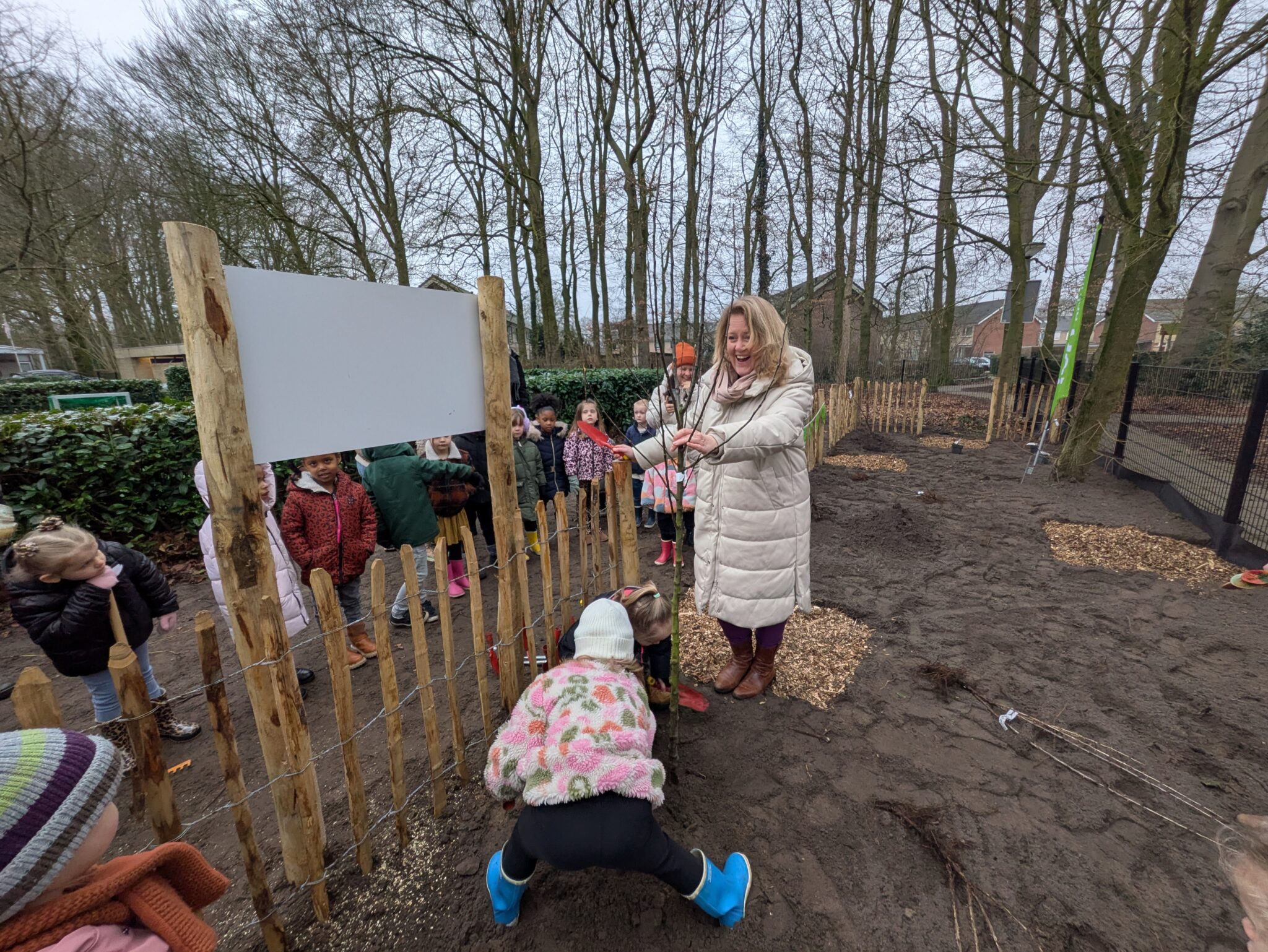 Kinderen en een volwassene planten een boom in een bosrijke omgeving.