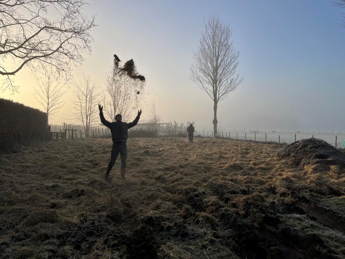 Persoon gooit aarde omhoog in een veld bij zonsopgang; mistige achtergrond met bomen.