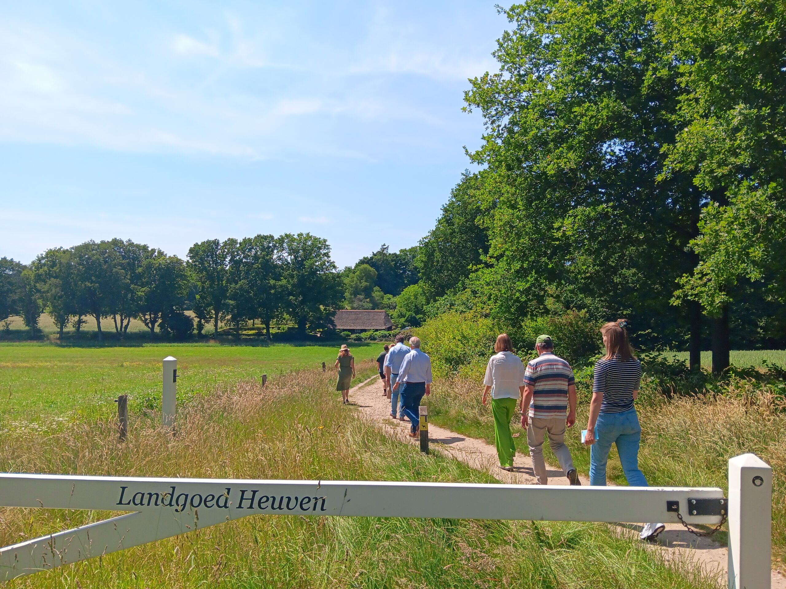 Mensen wandelen op een pad bij Landgoed Heuven, omringd door groene velden en bomen.
