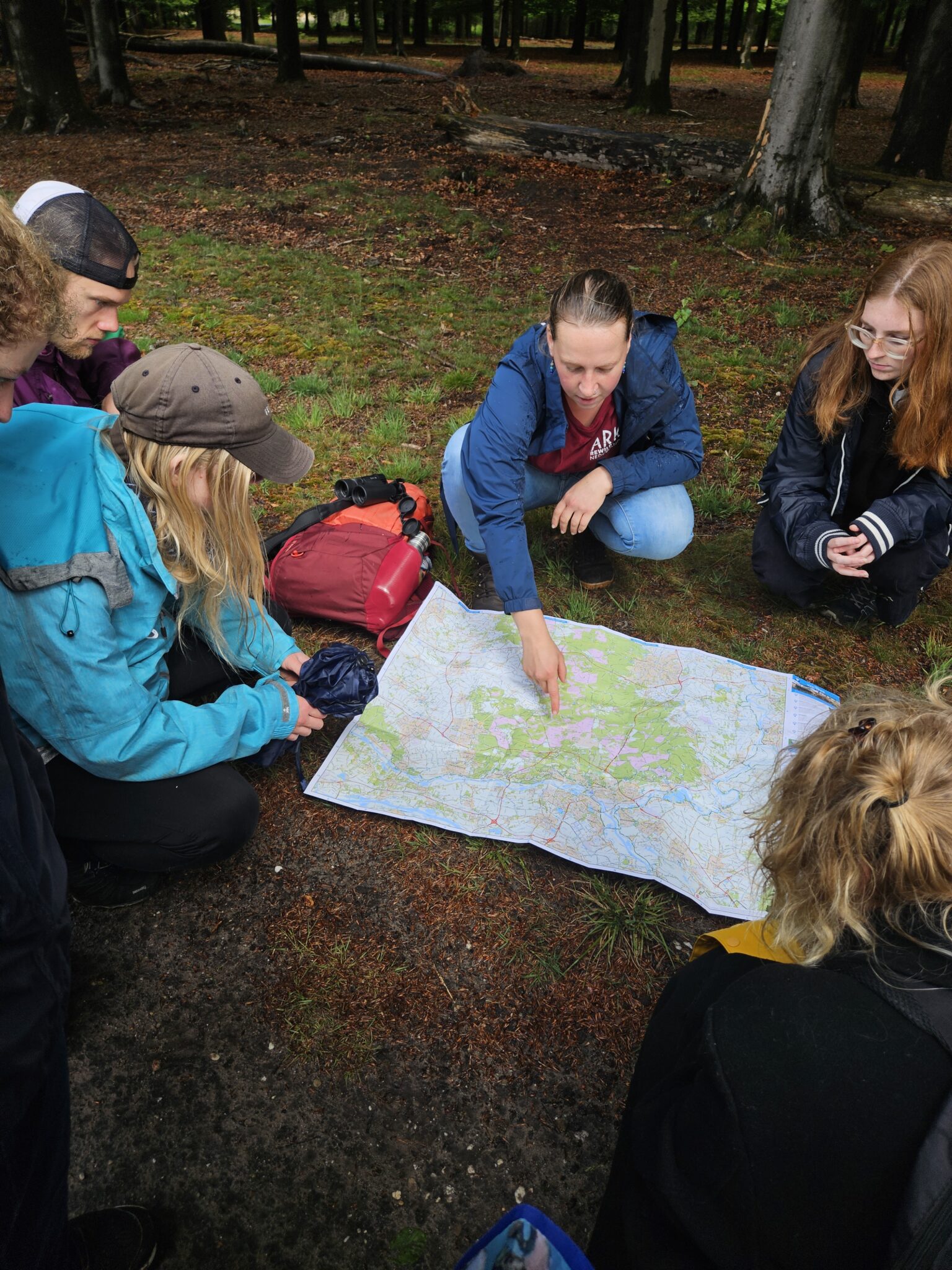 Groep mensen zit in bos en bekijkt samen een kaart op de grond.