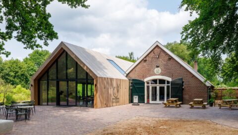 Modern natuurcentrum met glazen gevel en houten afwerking, omringd door groene bomen.