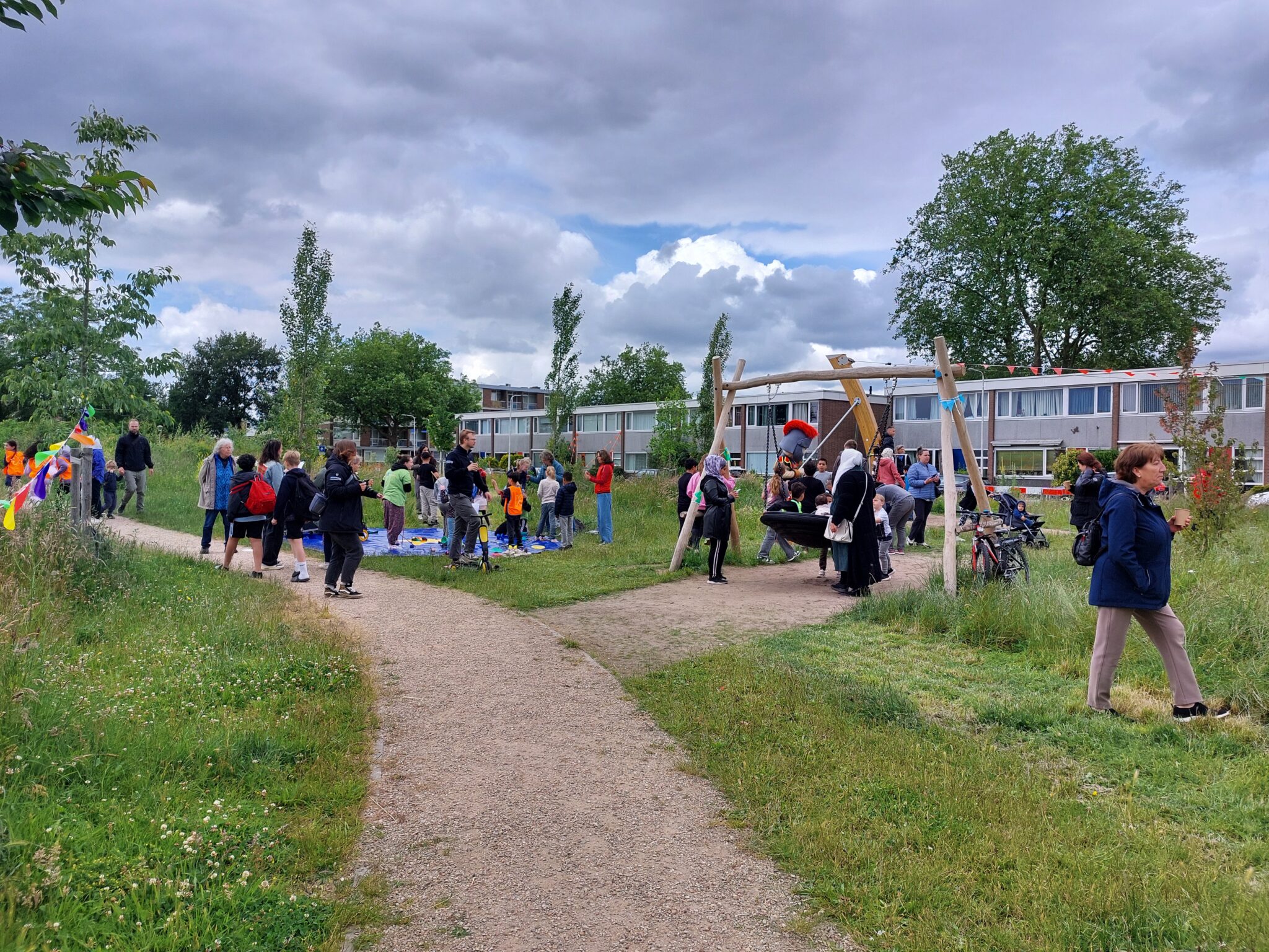 Mensen verzamelen zich in een park bij een speeltoestel, onder een bewolkte lucht.