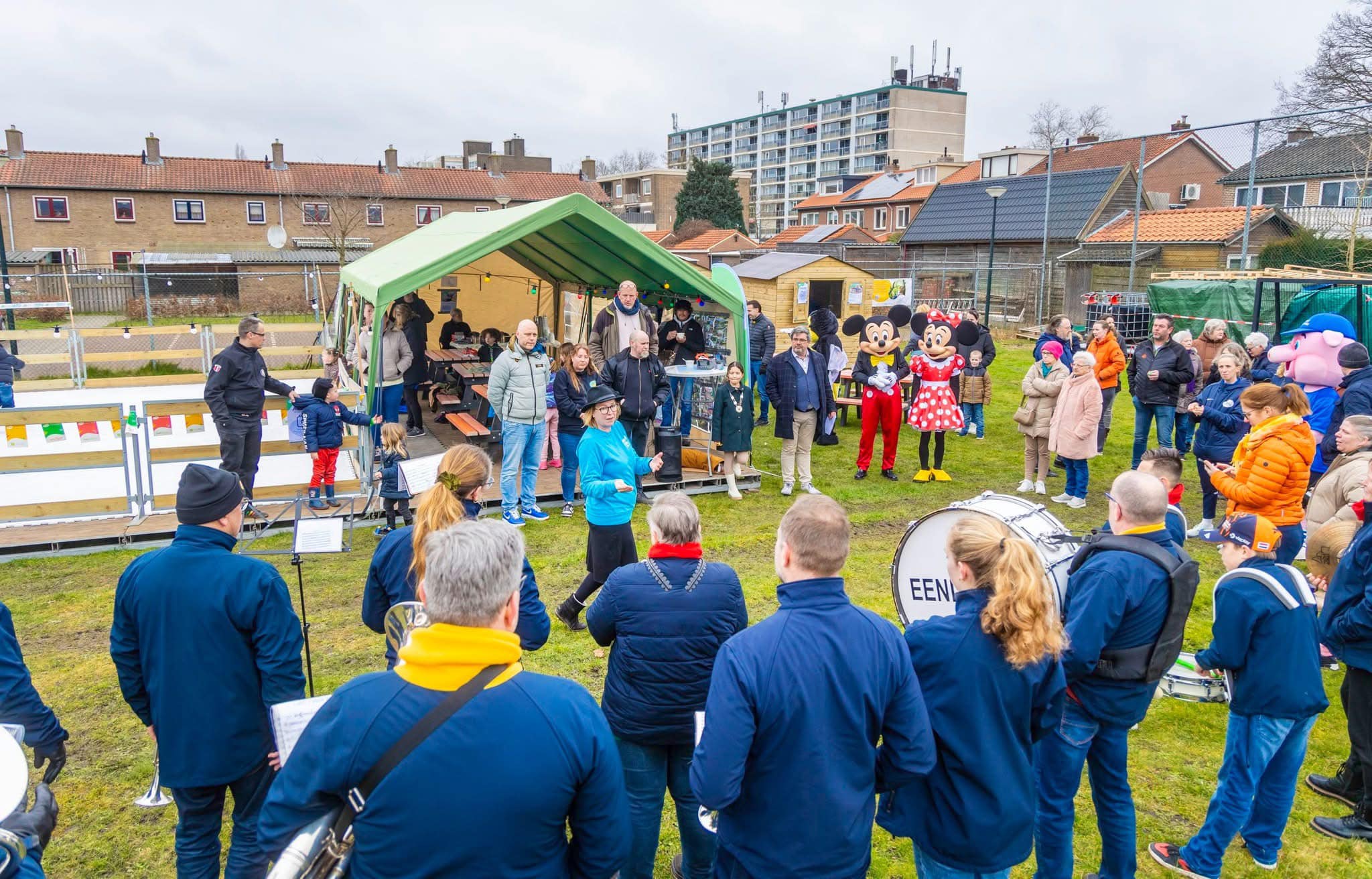 Groep mensen verzameld bij een feestelijke gebeurtenis met muziekoptredens en cartoonfiguren.