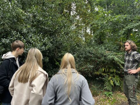 Groep mensen luistert aandachtig naar gids in een groen bos.